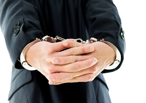 Businessman hands in handcuffs behind his back.