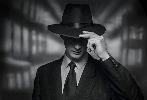 The detective takes on the camera. Vintage style black and white image of a polite young man in a suit doffing his hat in acknowledgement or greeting