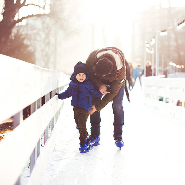 Father and son on ice skating Father is learning his 4 years old son how to skate on ice. They are outdoor in the city ice skating park.  Kid is enjoying it. ice skating photos stock pictures, royalty-free photos & images
