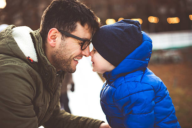 Father and son doing nose kissing at the ice-skating. They are laughing.