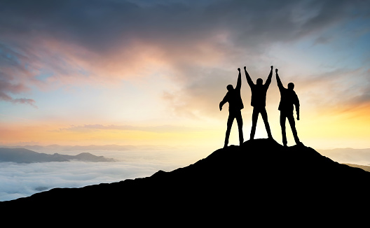 Silhouette of the team on the peak of mountain. Sport and active life.