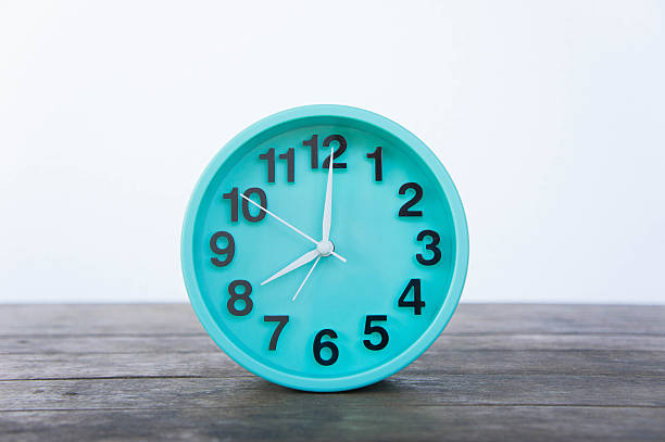 istock Green clock on a wooden table on a white background. 635781920