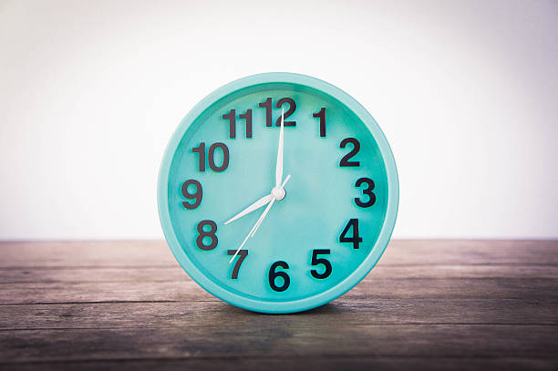 istock Green clock on a wooden table on a white background. 635781956