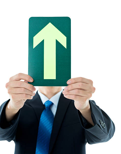 Businessman holding a green upward arrow against white background.