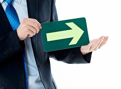 Businessman holding a green arrow forward against white background.