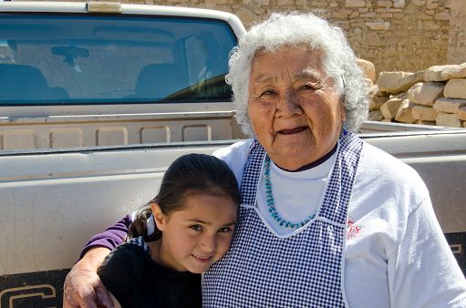 Acoma Pueblo, United States - March 19, 2016: The Acoma Pueblo sits on a mesa 365 feet above the desert floor, with no running water or electricity available.  Having been consistently inhabited since the early 13th century, currently there are about 300 adobe and stucco homes there, with 30 year round residents.  This Native American tribe has  approximately 5,000 members today, with the little pueblo's population swelling on the weekends with family members visiting their ancestral homes and tourists taking part in guided tours.  Pictured here is a pottery artist with her young granddaughter.