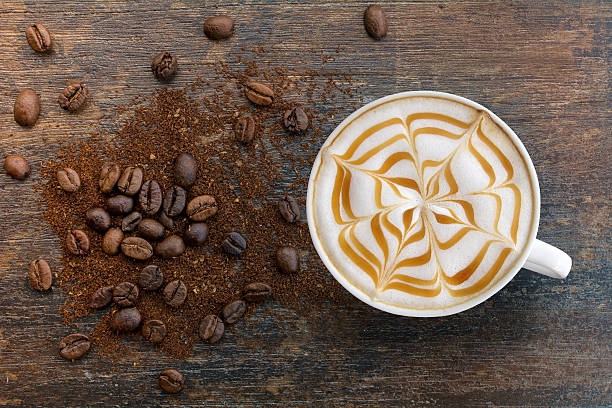 Caramel cappuccino with ground top view. Hot Cappuccino coffee with zigzag caramel motif or spiderweb art floating on top and coffee beans with ground on wooden background. Coffee break at retro style coffee shop,t op view. froth decoration stock pictures, royalty-free photos & images