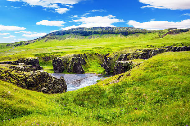 The concept of active northern tourism. The striking canyon in Iceland. Bizarre shape of cliffs surround the stream with glacial water. Green Tundra in July
