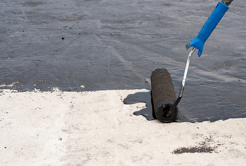 Roofer worker painting black coal tar or bitumen at concrete surface by the roller brush, A waterproofing.