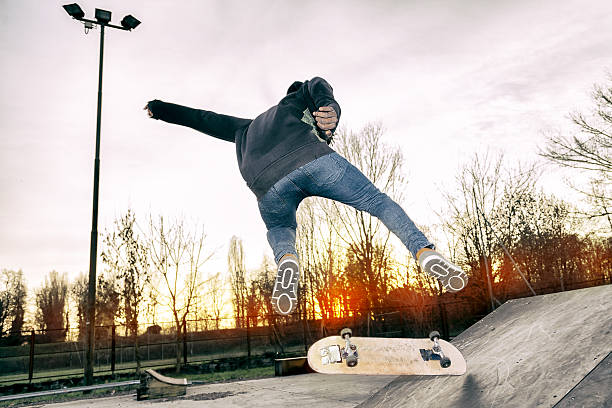 A young adult skater jumping with his skateboard at the skatepark.