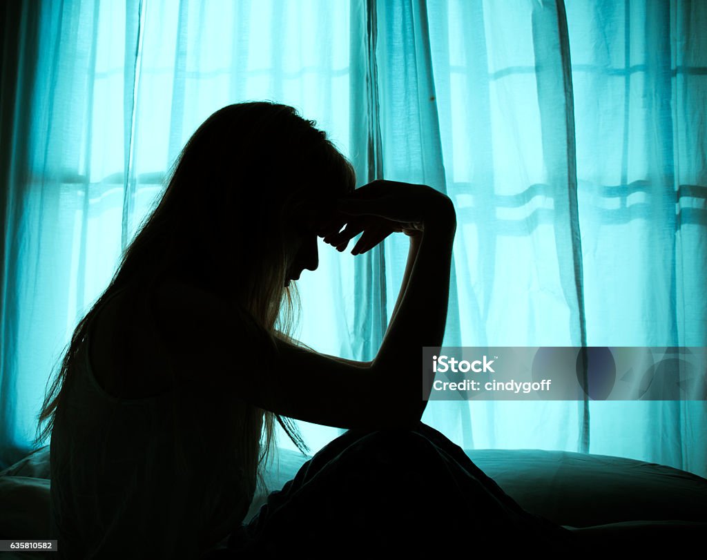 Silhouette of woman sitting in bed by window Women Stock Photo