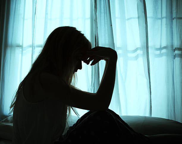 Silhouette of woman sitting in bed by window Silhouette of woman sitting in bed by window headache photos stock pictures, royalty-free photos & images