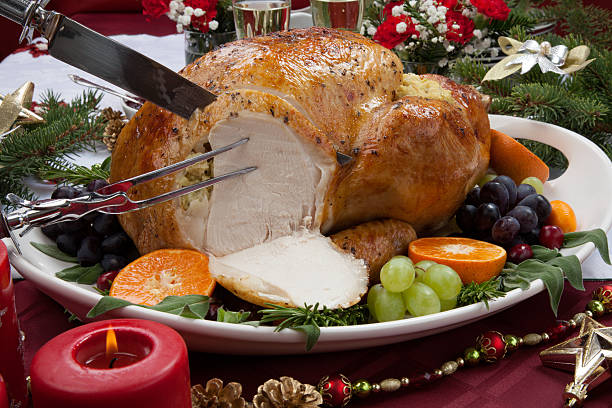 Carving Roasted Turkey for Christmas Dinner Carving roasted herb rubbed turkey garnished with fresh grapes, oranges, and cranberry is ready for Christmas dinner. Ornaments, Champagne, candles, and other Christmas decorations on feast table. carving food photos stock pictures, royalty-free photos & images