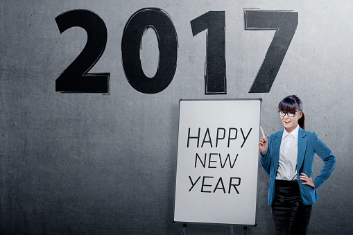 Young asian business woman with Happy New Year's greeting over 2017 number on the grey wall