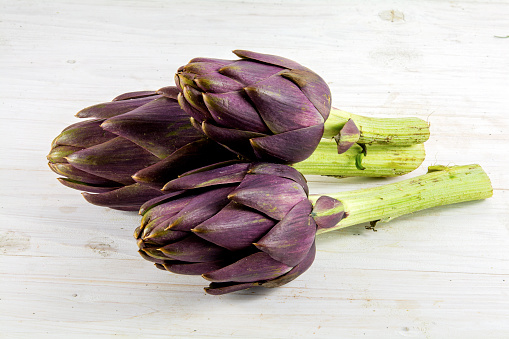 three purple artichokes from italy on white rustic wood, selective focus