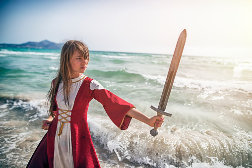 Young viking shieldmaiden practicing with sword on the beach. 