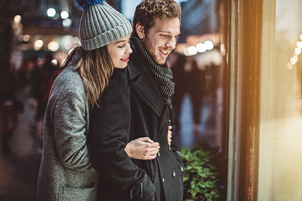 Strolling thru the city Couple window shopping outdoors in winter city street. Standing in front of a store window and looking inside. Wearing warm clothing. window shopping at night stock pictures, royalty-free photos & images