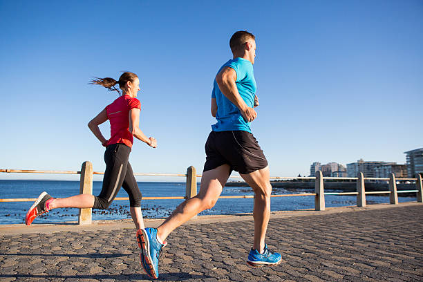 A large group of multi-ethnic men and women go on a run together outside.  They are each dressed comfortably in athletic wear and smiling as they enjoy the fresh air on a sunny summer day.