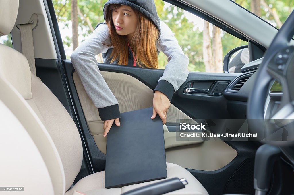 Woman burglar steal a laptop through the window of car Woman burglar steal a laptop through the window of car - theft concept Car Stock Photo