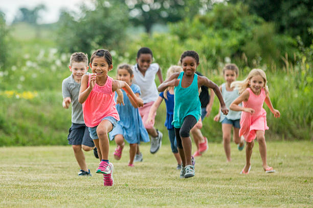 Playing Outside in a Field on a Sunny Day A multi-ethnic group of elementary age children are playing together outside at recess. They are chasing each other and are playing tag. playful stock pictures, royalty-free photos & images