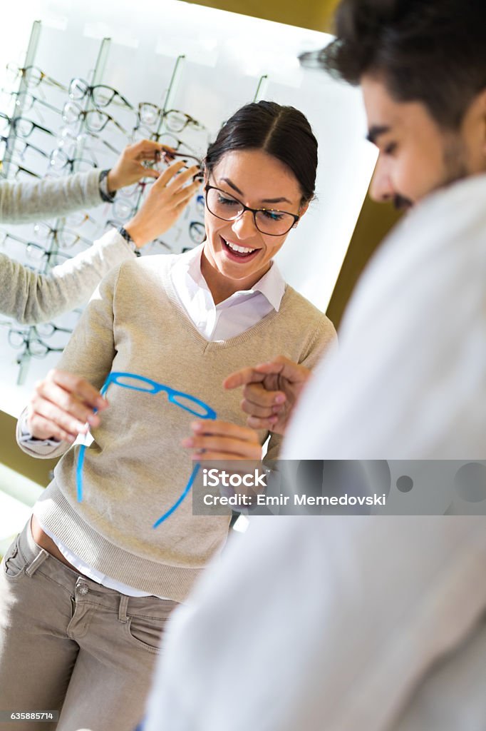 Woman selecting eyeglasses in optical store Cheerful woman is selecting eyeglasses in optical store with the assistance of her optometrist. Optometrist Stock Photo