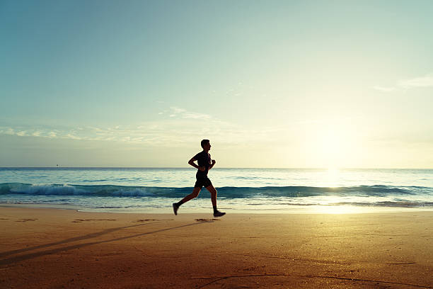 człowiek działa na tropikalnej plaży o zachodzie słońca - sun people jogging sunset zdjęcia i obrazy z banku zdjęć