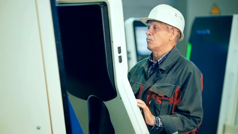 Worker at workshop operating industrial machine by computer