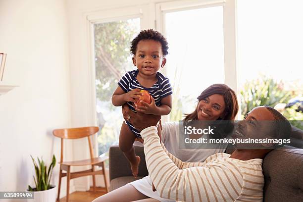 Parents And Son Playing Game On Sofa At Home Stock Photo - Download Image Now - Family, Baby - Human Age, African-American Ethnicity