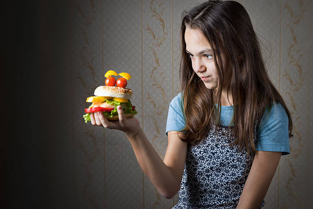 girl holding at arm hamburger decorated as smiley face 11 year old girl holding at arm hamburger decorated as smiley face with eyes of cherry tomatoes, and looks at it. gawp stock pictures, royalty-free photos & images