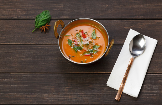 Vegan and vegetarian dish, spicy creamy tomato dahl soup bowl. Indian cuisine, masala hot meal on wood background. Eastern local cuisine restaurant food above view