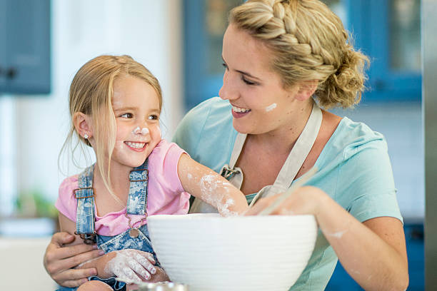 A mother and daughter are baking together in the kitchen on mother's day. They are mixing flour and making a miss in the kitchen.