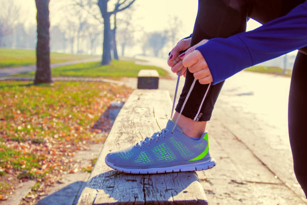 unrecognizable young runner tying her shoelaces - shoe tying adult jogging imagens e fotografias de stock