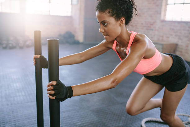 African woman doing intense workout in gym Side view shot of fit young woman pushing the sled at gym. African woman doing intense physical workout in gym. prowling stock pictures, royalty-free photos & images