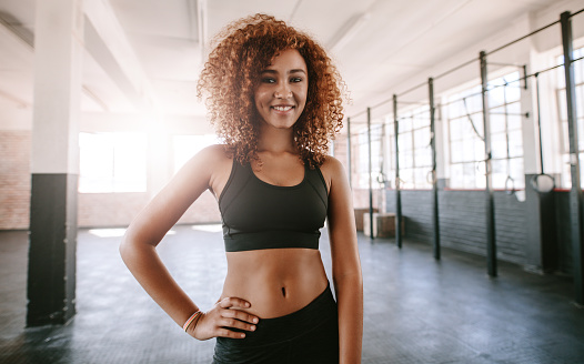 Portrait of beautiful young african woman in gym. Fitness model posing in the gym and smiling.
