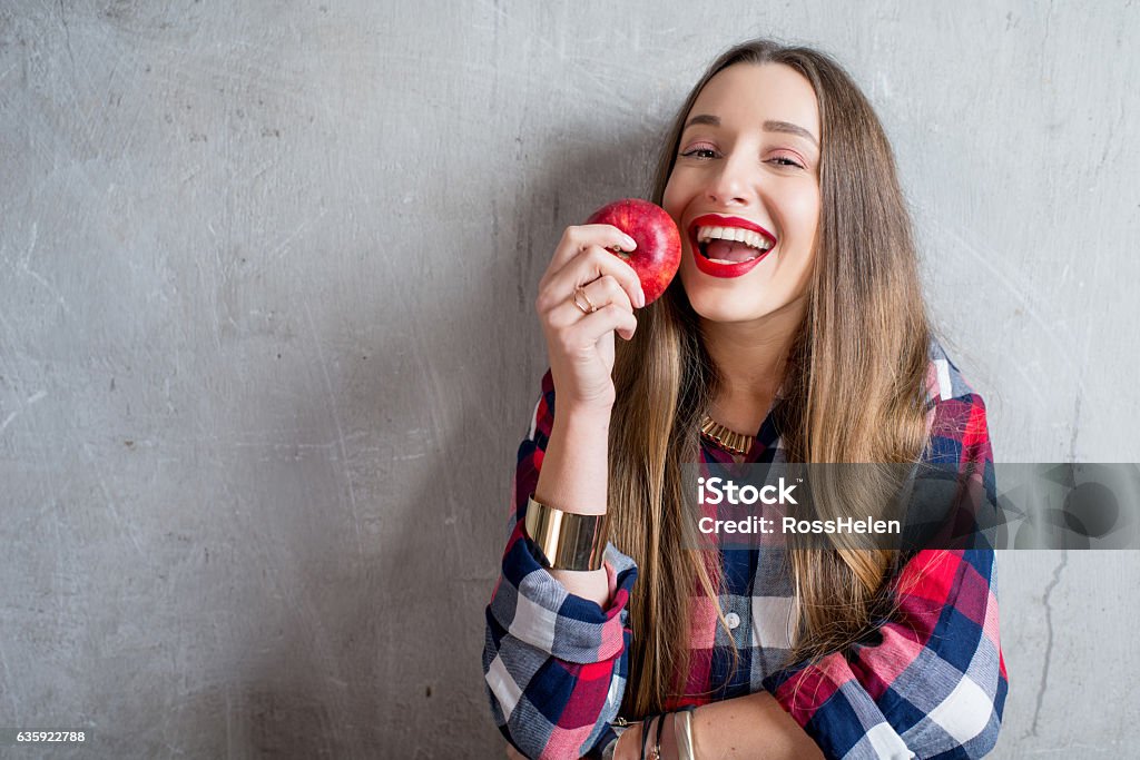 Woman with apple on the gray background Young woman with toothy smile and red apple on the gray wall background Apple - Fruit Stock Photo