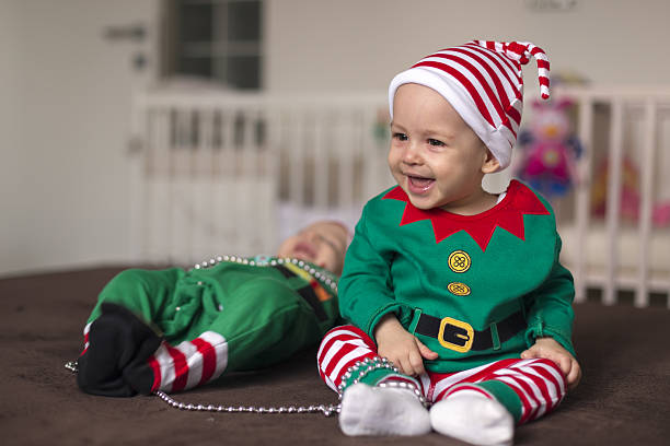 Happy twin babies elf helper of Santa in costume at home in living room