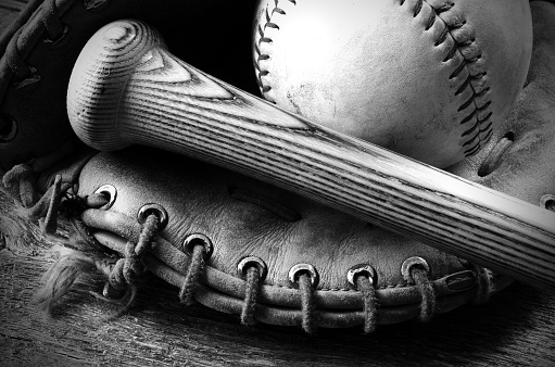 A black and white image of an old baseball glove and bat.