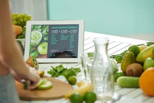 Woman reading green smoothie formula on tablet when cooking