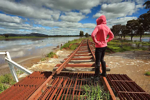 A female looks out over the floodwaters from the buckled train tracks at Crowther, Hilltops Region, Country NSW.