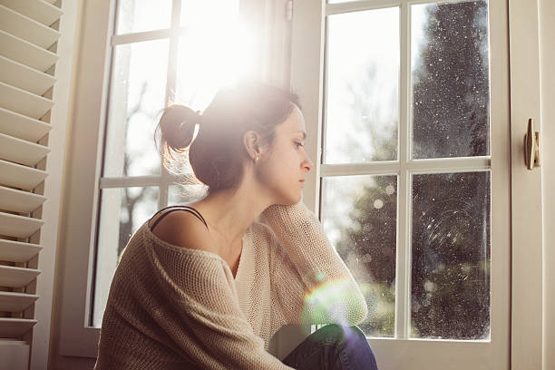 casalinga infelice seduta vicino alla finestra - women sadness depression fear foto e immagini stock