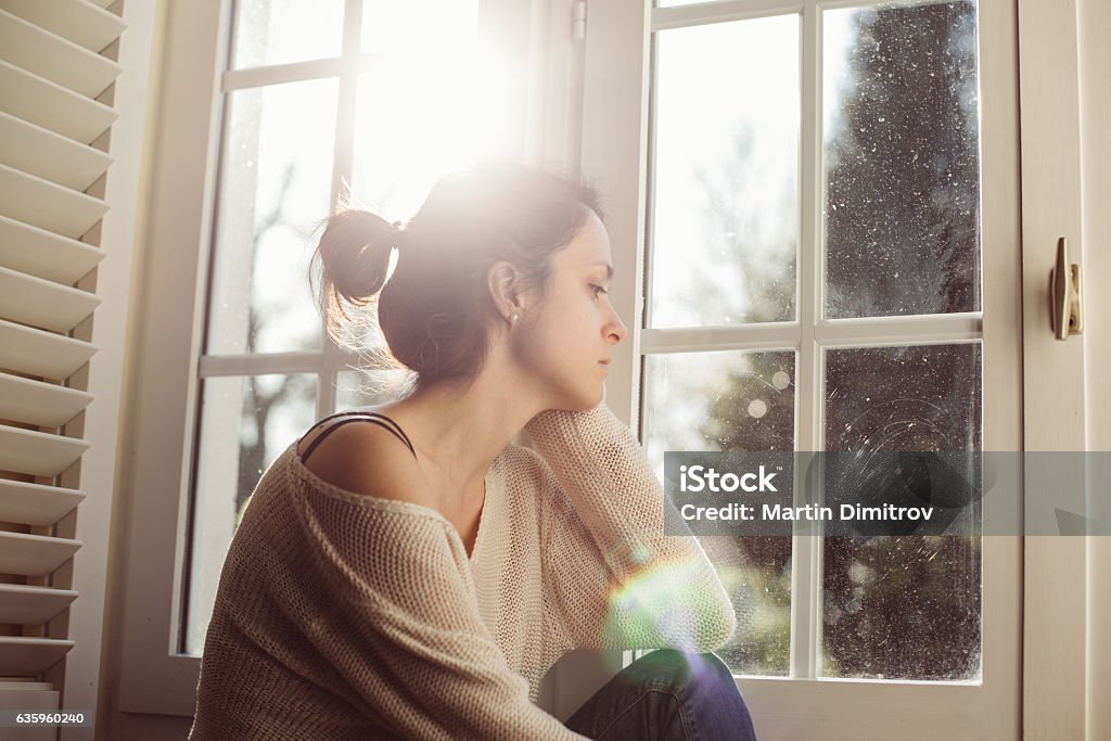 Unhappy housewife sitting near the window Thoughtful woman at home - copyspace Women Stock Photo