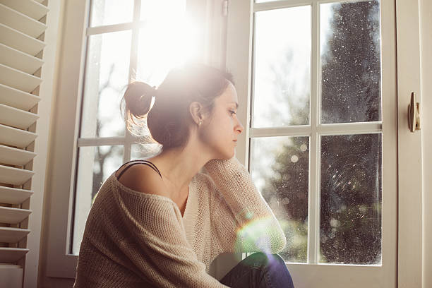 unhappy housewife sitting near the window - stereotypical housewife depression sadness women imagens e fotografias de stock