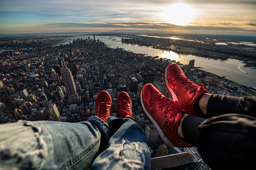 POV image of Manhattan island in New York City during helicopter flight. Sunset is seen in the background and human legs in front view.