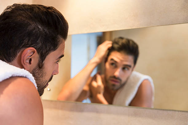 istock Young man examining himself in bathroom mirror 635966370
