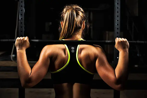 Photo of Back view young adult girl doing barbell squats