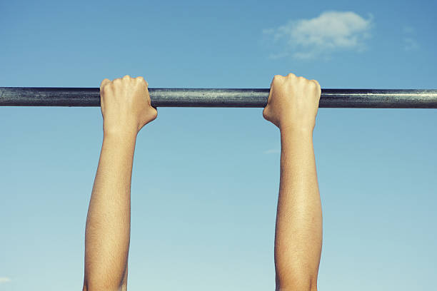 Person hanging on horizontal bar Person hanging on horizontal bar against sky. horizontal bar stock pictures, royalty-free photos & images