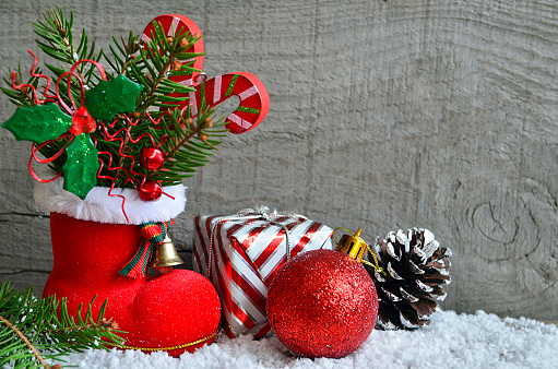Red Santa's boot with fir tree branch,holly berry leaves,candy cane,pine cone,gift and red bauble.Christmas decoration.Xmas background.Selective focus.Merry Christmas or Happy New Year concept.