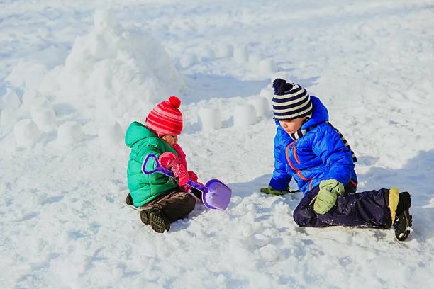 istock little boy and girl digging snow in winter 635983548