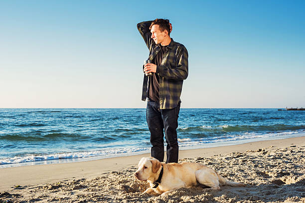 istock young caucasian male drinking coffee on beach, walking with dog 635984724