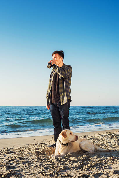 istock young caucasian male drinking coffee on beach, walking with dog 635984952